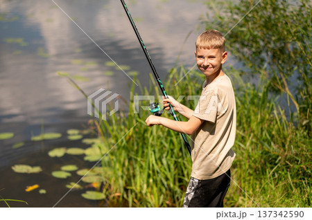 Happy blond boy fishing on river bank, enjoying summer outdoor activity in nature 137342590