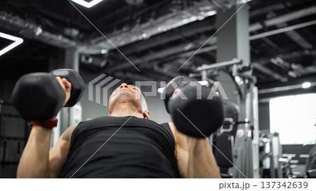 Man lifting dumbbells during strength training in gym 137342639