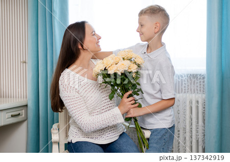 Teenage boy hugging mother and giving bouquet of yellow roses for Mother's Day at home Teenage boy hugging mother and giving bouquet of yellow roses for Mother's Day at home 137342919