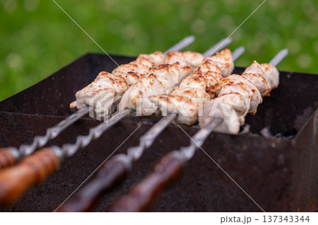 Shashlik on skewers grilling over charcoal in summer day 137343344