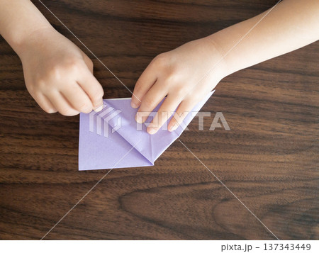 木のテーブルで紫の折り紙を折る子どもの手 木のテーブルで紫の折り紙を折る子どもの手 137343449