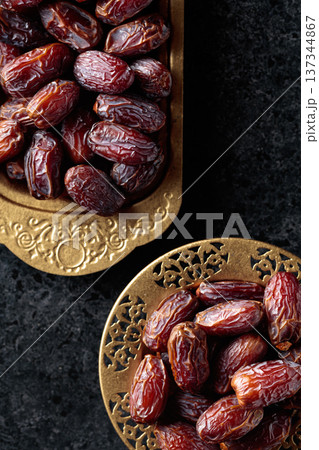 Dates fruits in a golden bowls on black stone table. 137344867