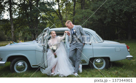 Elegant bride and groom celebrating their wedding day with a vintage car in a picturesque outdoor setting 137344901