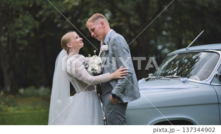 Newlywed couple embracing near vintage wedding car, soft romantic light highlighting intimate connection and wedding day joy 137344902