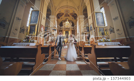 Loving newlyweds exiting church sanctuary, holding hands and smiling after exchanging marriage vows Loving newlyweds exiting church sanctuary, holding hands and smiling after exchanging marriage vows 137344903