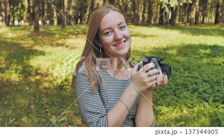 Young photographer smiling and holding a camera in a park, enjoying her passion for photography in nature Young photographer smiling and holding a camera in a park, enjoying her passion for photography in nature 137344905