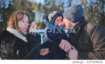 Happy family feeding tangerine segments to young child during bright winter afternoon outside Happy family feeding tangerine segments to young child during bright winter afternoon outside 137344918