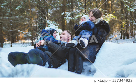 Family enjoying a joyful winter day, playing together in the snow amidst a beautiful forest filled with sunlight and frosty trees 137344922
