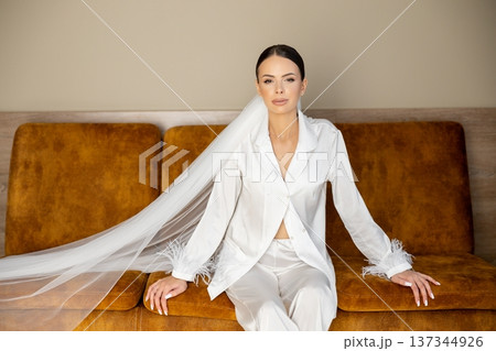 Bride relaxing on sofa wearing white pajamas and veil Bride relaxing on sofa wearing white pajamas and veil 137344926