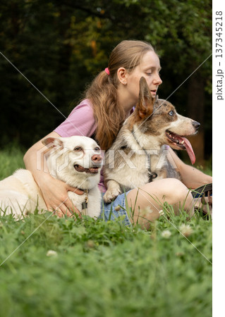 Professional dog walker young woman with pack of dogs is sitting on grass and enjoying walk animals. 137345218