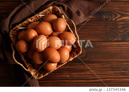 Rustic woven basket filled with fresh brown eggs, placed on wooden background 137345346