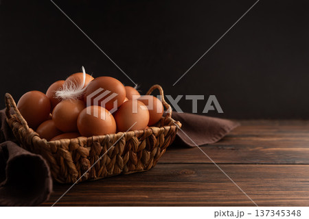 Rustic woven basket filled with fresh brown eggs, placed on wooden background with soft cloth and delicate white feather resting on top Rustic woven basket filled with fresh brown eggs, placed on wooden background with soft cloth and delicate white feather resting on top 137345348