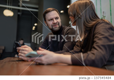 Man and woman working together on laptops at wooden benches with potted plants in bright indoor space. Office teamwork, laptop task, plants, indoor, business. 137345484