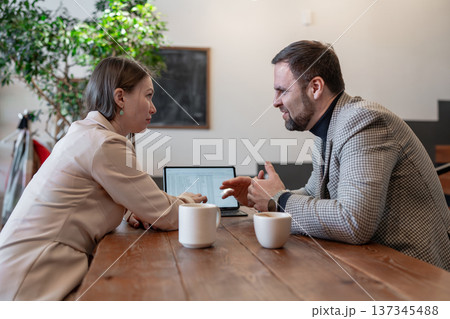 Colleagues planning project and reviewing paperwork together at cafe table with large window. Project planning, paperwork, table, teamwork, discussion. 137345488