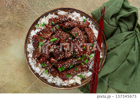 crispy beef, with green onions and sesame seeds, on a rice pad, in a bowl with chopsticks, on a textured surface, no people crispy beef, with green onions and sesame seeds, on a rice pad, in a bowl with chopsticks, on a textured surface, no people 137345673