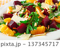 Fresh salad with beets, oranges, and arugula topped with cheese and nuts served on a white plate 137345717