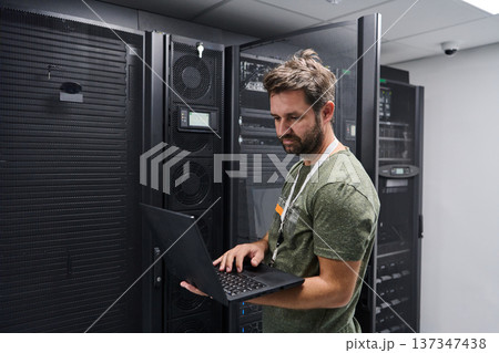 It technician working on laptop in server room performing network maintenance and hardware monitoring It technician working on laptop in server room performing network maintenance and hardware monitoring 137347438