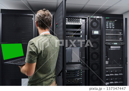 Data center technician using laptop to check server rack and network equipment in a server room 137347447