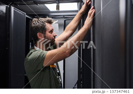 IT technician inspecting server rack in data center performing maintenance and hardware installation IT technician inspecting server rack in data center performing maintenance and hardware installation 137347461