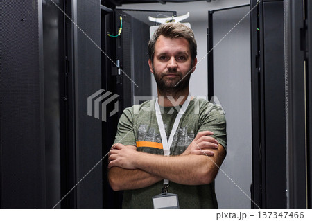 Confident data center technician standing with arms crossed between server racks in a modern IT room Confident data center technician standing with arms crossed between server racks in a modern IT room 137347466