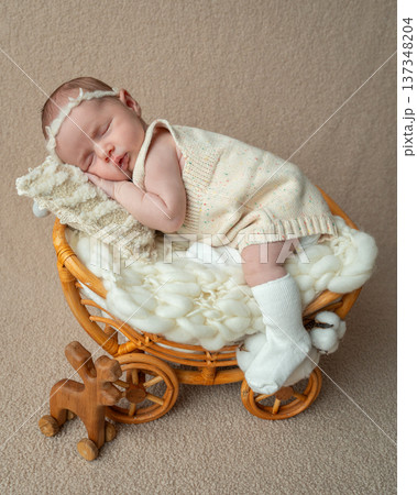 Full body portrait of a newborn baby girl sleeping in a wicker basket bed. Neutral tones and soft fabrics create a cozy atmosphere symbolizing family warmth and parental love 137348204