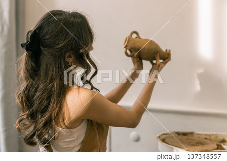Young female ceramic artist holding handmade clay vase in pottery studio, creative craft process and handmade ceramics production 137348557