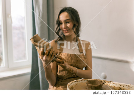 Young female ceramic artist holding handmade clay vase in pottery studio, creative craft process and handmade ceramics production 137348558