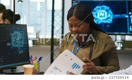 Joyous technician with disability and coworker chatting while coding AI algorithms debugging software issues. Upbeat tech startup office IT expert in wheelchair and colleague using computer, camera A 137350514
