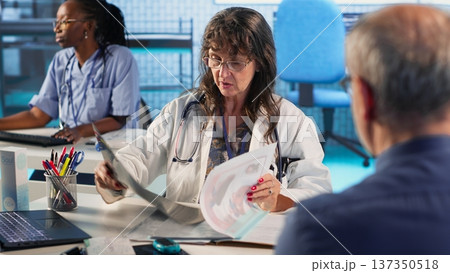 Old sick person discussing about diagnostic results and recovery plan with physician during check up, using advanced tech to get correct lab results. Patient care on health insurance. Camera B. 137350518