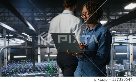 Data center engineer walking on industrial platform, running diagnostics on equipment to identify errors. Server farm IT professionals preventing rigs failure to minimize downtime Data center engineer walking on industrial platform, running diagnostics on equipment to identify errors. Server farm IT professionals preventing rigs failure to minimize downtime 137350544