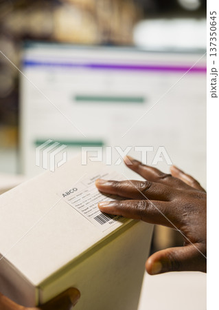 Close up of worker managing package labeling using shipment details adhesive tags, handling order processing and preparing the goods for delivery. Online shopping fulfillment center. 137350645