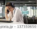 Tired programmer in Silicon Valley company office listening music to destress. Exhausted IT specialist wearing headphones closing eyes to relax at work while debugging applications 137350650