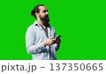 Casual stylish guy browsing his smartphone against green screen background, connected online on social network platforms or texting messages. Young adult focused on social media apps. Camera A. 137350665