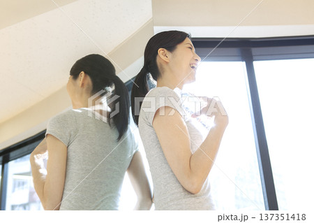 ペットボトル持って窓際に立つ女性 137351418