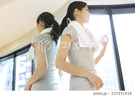 ペットボトル持って窓際に立つ女性 137351419