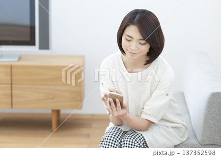 リビングでスマートフォンを操作する女性 リビングでスマートフォンを操作する女性 137352598