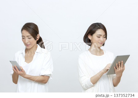 タブレットとスマートフォンを操作する母親と娘 137352734