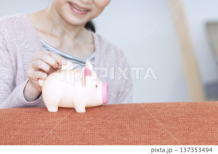 貯金箱にお金を入れる女性 137353494