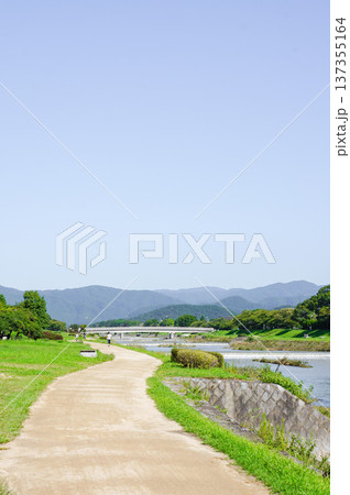青空と緑の中を進む川沿いの散歩道 137355164