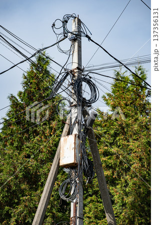Overloaded utility pole with tangled cables and wires for power and communication 137356131