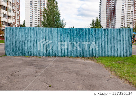 Weathered teal wooden fence against urban high-rise buildings and cloudy sky Weathered teal wooden fence against urban high-rise buildings and cloudy sky 137356134