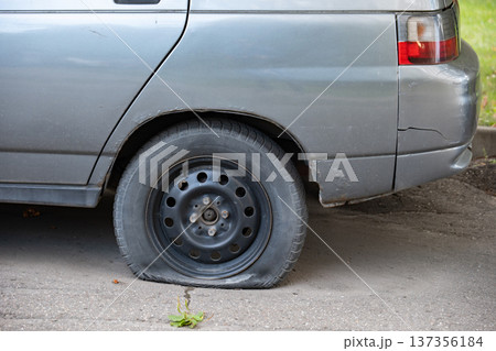 Old gray car with a flat, deflated rear tire on asphalt, needing repair Old gray car with a flat, deflated rear tire on asphalt, needing repair 137356184