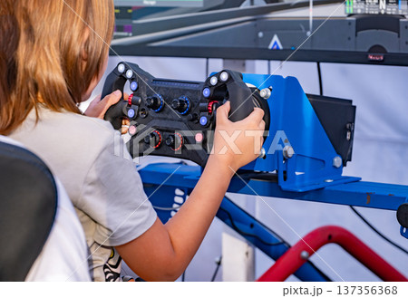 Young boy playing a racing simulator steering wheel, enjoying competitive video game Young boy playing a racing simulator steering wheel, enjoying competitive video game 137356368