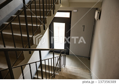 Empty concrete staircase with dark metal railings leading to a light-filled door on the first floor landing. Empty concrete staircase with dark metal railings leading to a light-filled door on the first floor landing. 137356389