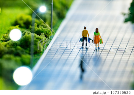 Miniature couple walking on sidewalk after shopping, carrying bags 137356626