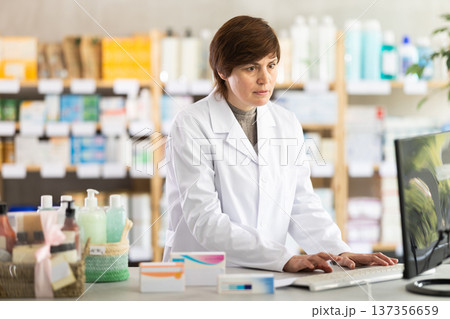 Female pharmacist working on computer at pharmacy counter Female pharmacist working on computer at pharmacy counter 137356659