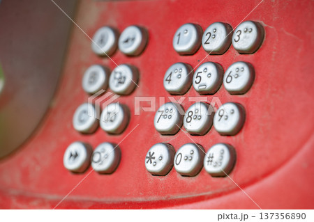 Close-up of dusty red payphone keypad with metal buttons, numbers, and Braille dots 137356890