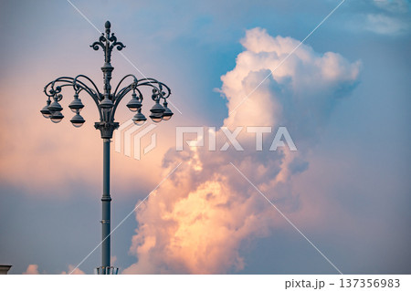 Vintage street lamp standing against a dramatic evening sky with warm sunset clouds 137356983