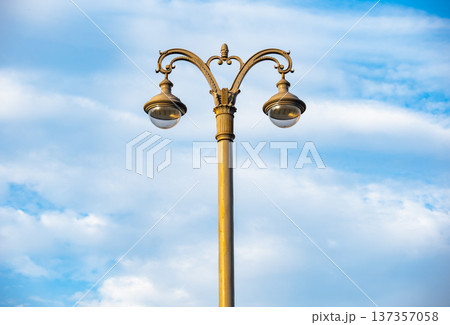 Vintage street lamp with ornate design against a bright blue sky with clouds Vintage street lamp with ornate design against a bright blue sky with clouds 137357058