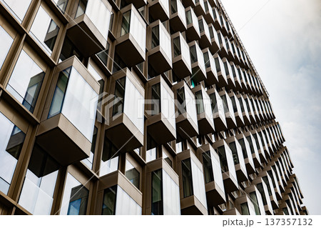 Modern building facade featuring geometric design with repeating square windows and sky reflections Modern building facade featuring geometric design with repeating square windows and sky reflections 137357132
